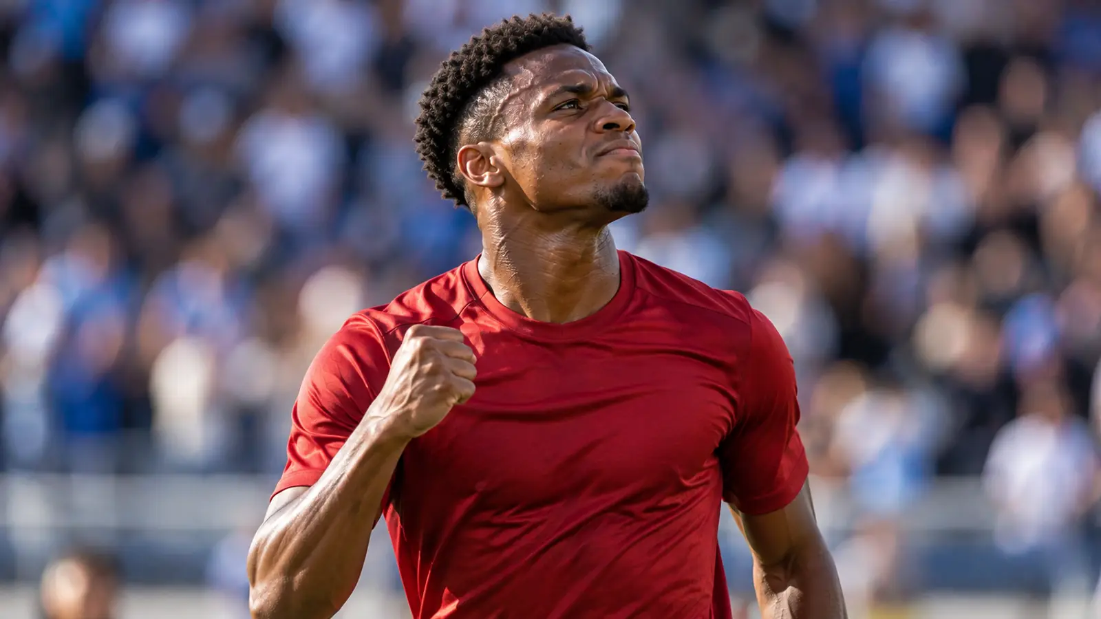 Un futbolista con equipación roja celebra un gol con el puño cerrado en un estadio de día