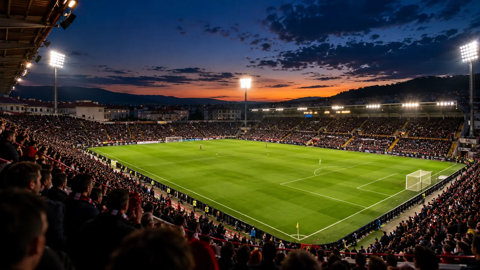 Estadio de futbol pequeno y lleno al atardecer con los focos encendidos antes de un partido